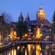An Amsterdam canal at dusk is lined with small boats and historic architecture